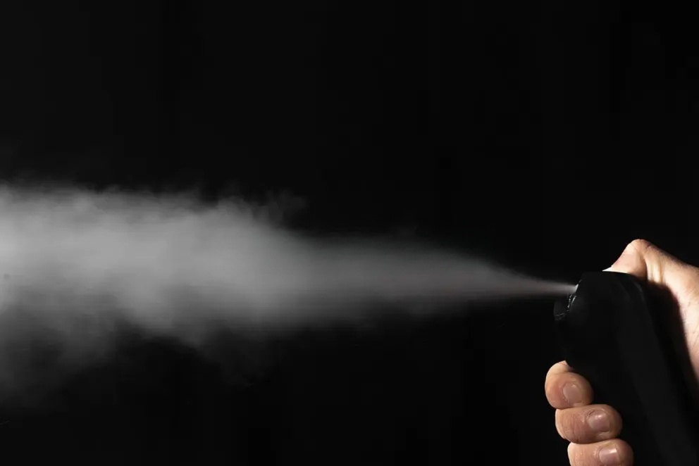 Close-up of a man spraying perfume mist from a bottle on a dark background